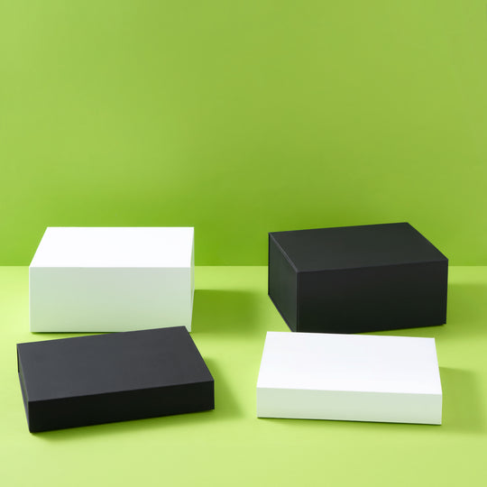 Four minimalist rectangular boxes in matte black and white, arranged on a light green surface against a solid lime green background.